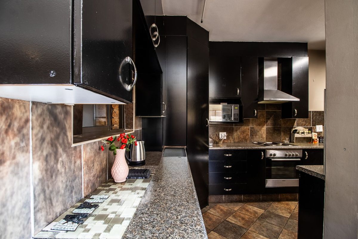 A functional kitchen featuring dark cabinetry, granite-style countertops, tiled backsplash, and built-in stainless steel oven and extractor fan.