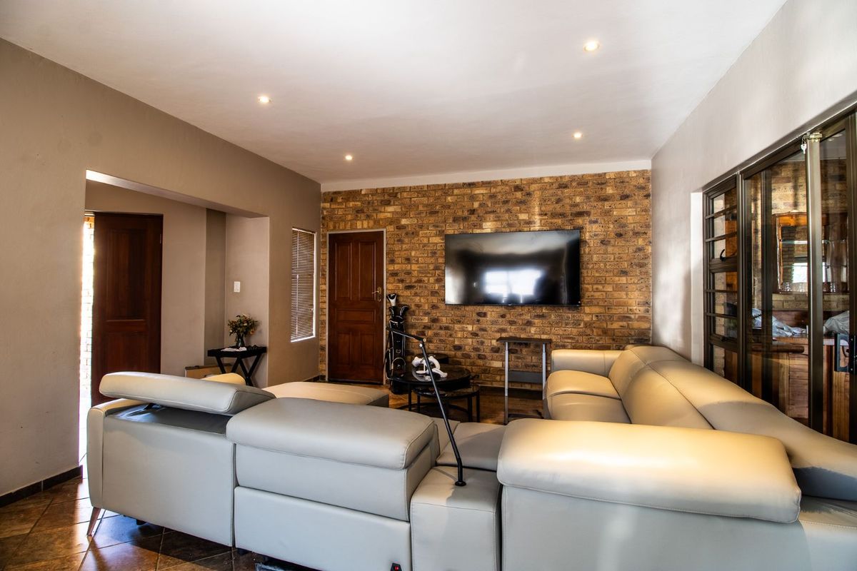 Spacious living room featuring a prominent exposed brick feature wall, recessed downlighting, and tiled flooring, creating a warm and inviting atmosphere.