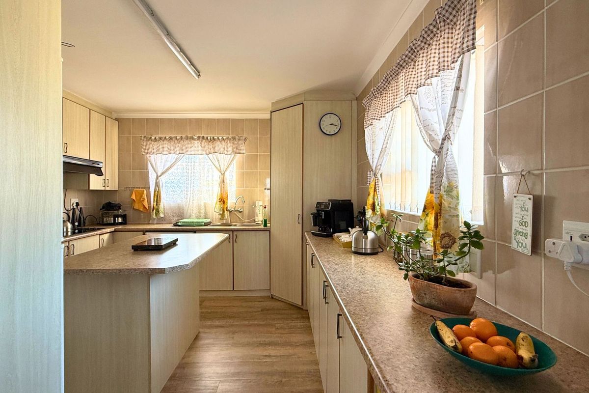 A functional kitchen featuring light-toned cabinetry, laminate countertops, tiled splashbacks, and a central island, providing ample workspace and storage.