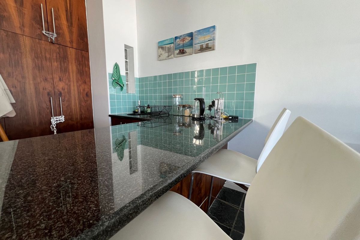 A kitchen area featuring a dark granite breakfast bar, teal square-tiled backsplash, and warm-toned wooden cabinetry.