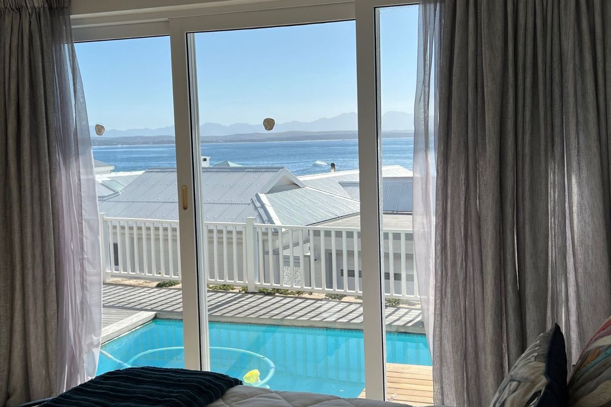 A bedroom view featuring large sliding glass doors that open onto a private deck with a swimming pool and scenic ocean views.