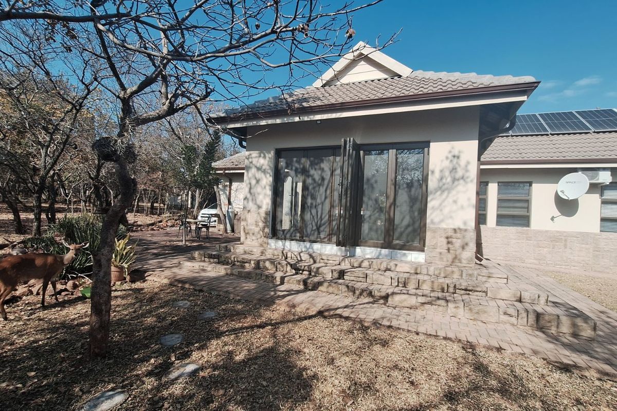 Rear view of the house featuring a paved patio area, stone cladding accents, and roof-mounted solar panels.