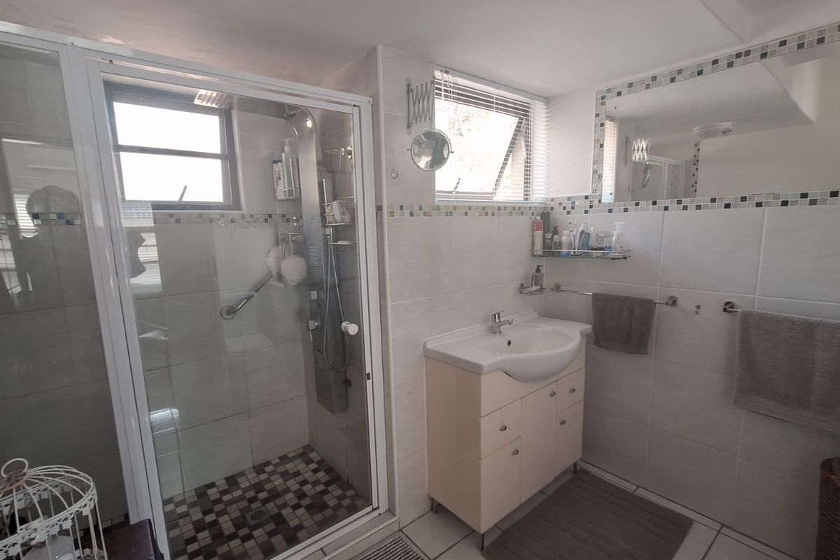 A functional bathroom featuring a glass-enclosed shower, a pedestal-style vanity with integrated basin, and neutral wall tiling with a decorative mosaic border.