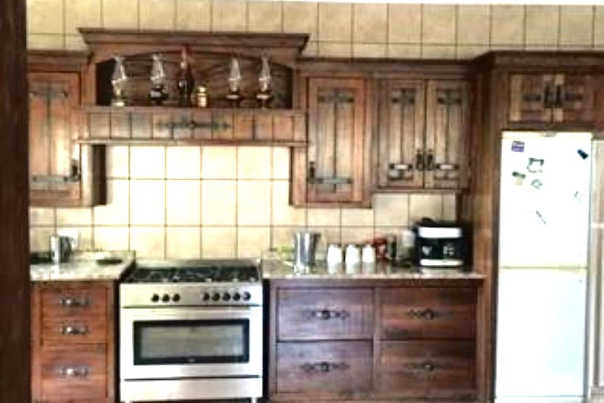 A rustic-style kitchen featuring dark wood cabinetry, tiled backsplash, and a stainless steel gas stove with an integrated extractor hood.