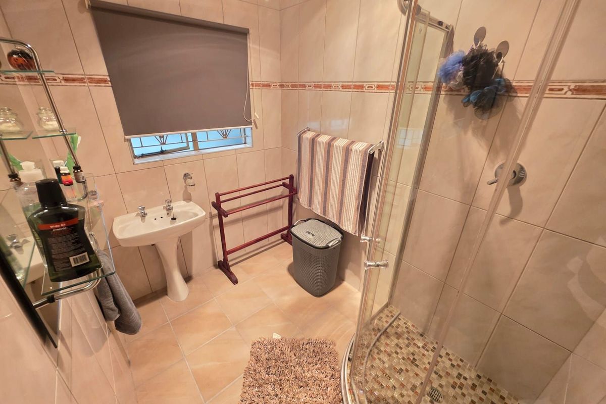 A functional bathroom featuring a corner glass shower enclosure, pedestal basin, and tiled walls and flooring.