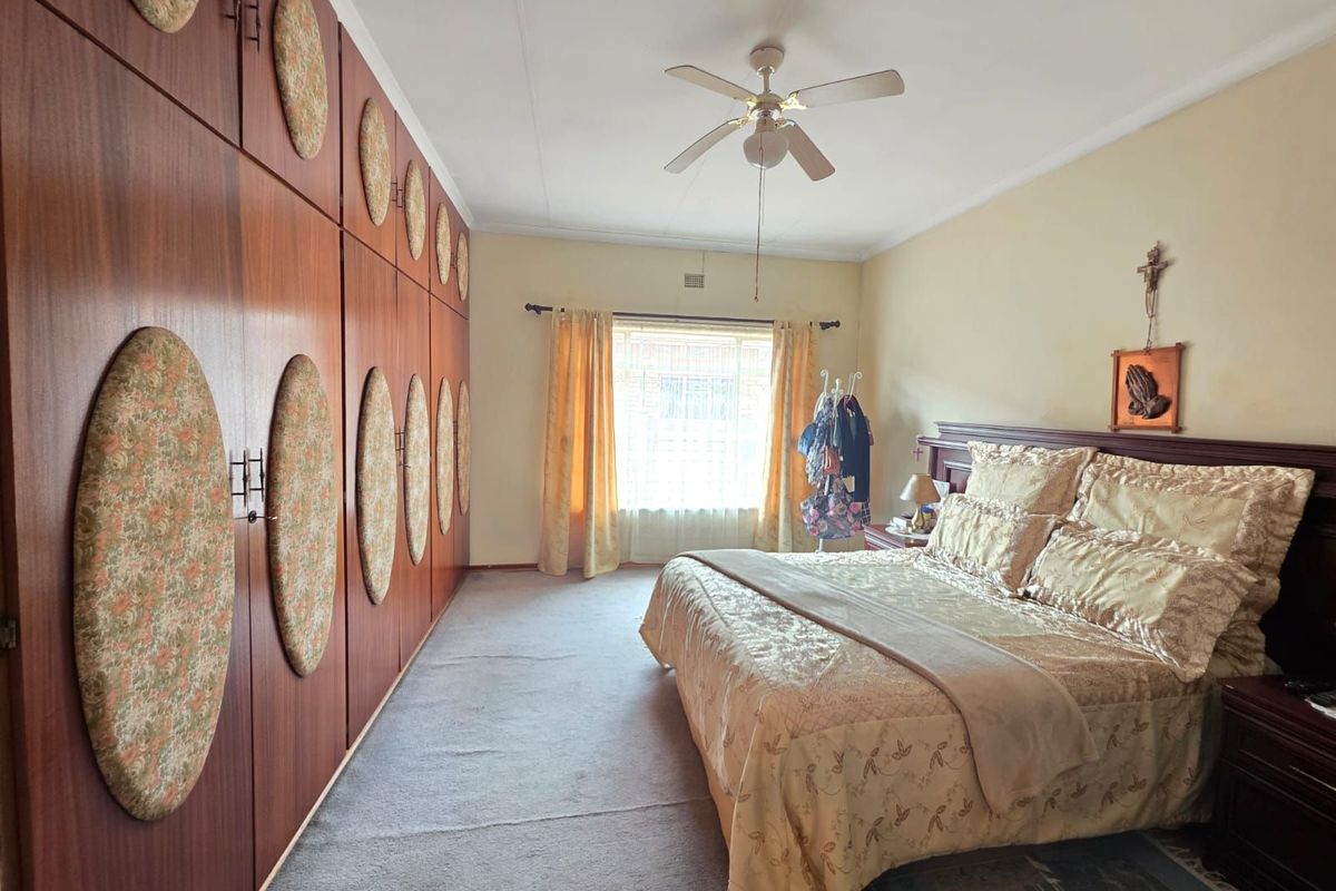 Spacious bedroom featuring extensive built-in wooden cabinetry, a ceiling fan, and large window providing natural light.