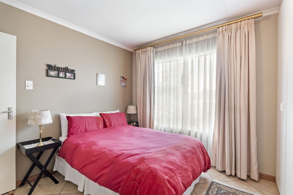 A well-lit bedroom featuring tiled flooring, neutral wall tones, and large windows dressed with floor-to-ceiling curtains.