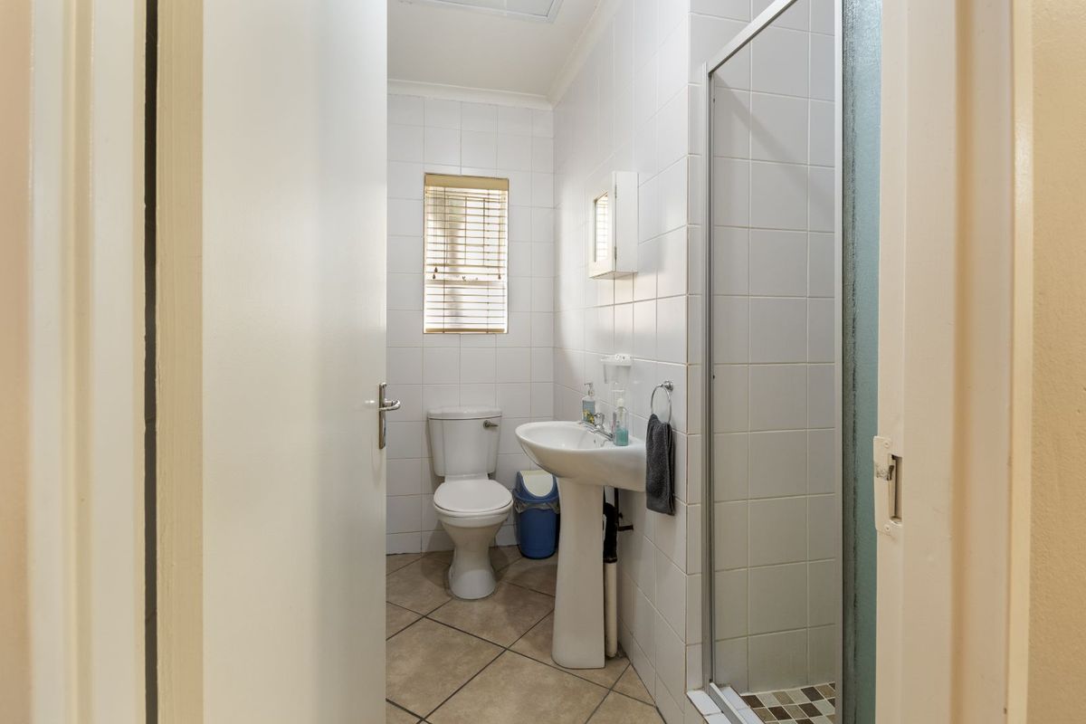 A functional bathroom featuring a pedestal sink, a toilet, and a glass-enclosed shower with white wall tiles and neutral floor tiling.