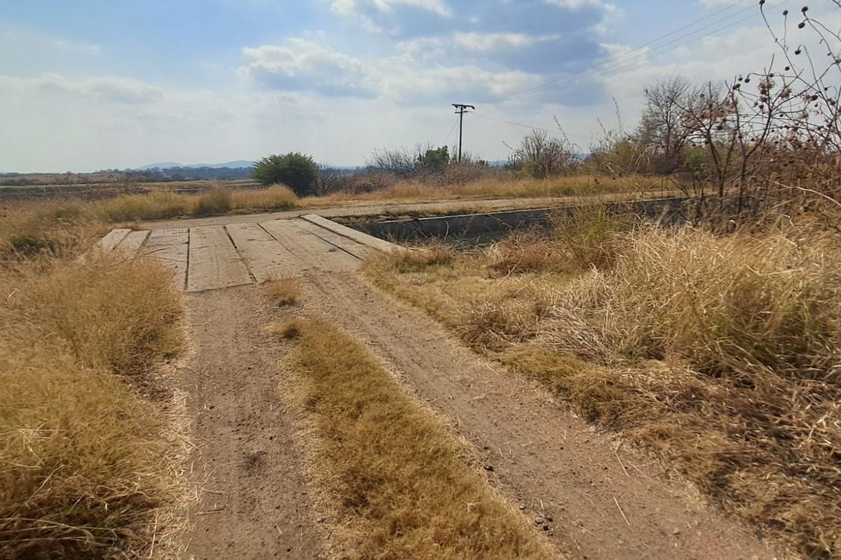 A rural farm access track leading to a concrete bridge crossing, set within an open landscape.