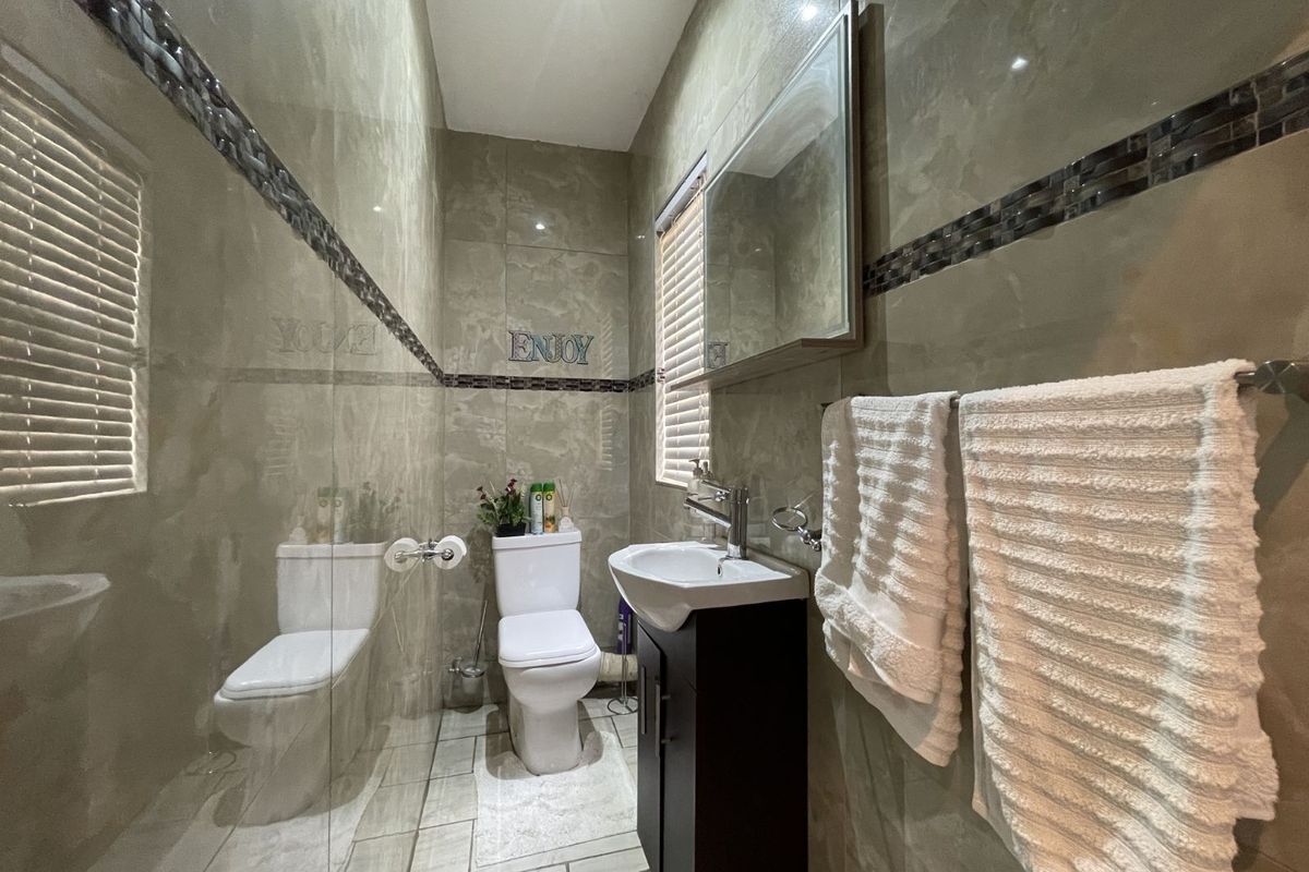 A modern bathroom featuring floor-to-ceiling tiled walls, a vanity basin with storage, a wall-mounted mirror cabinet, and a toilet.