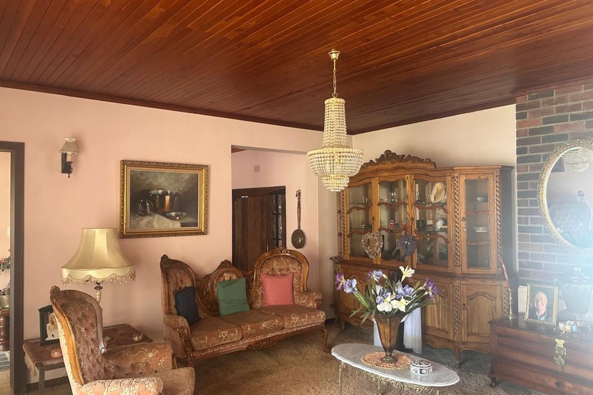 A traditional living room featuring a warm timber-paneled ceiling, a brick fireplace surround, and a classic crystal chandelier.