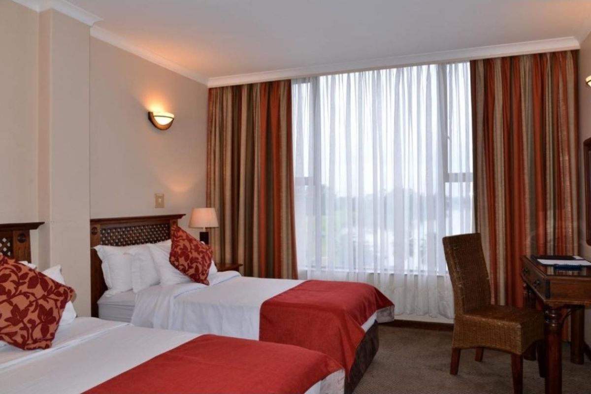 A hotel bedroom featuring a large window with natural light, wall-mounted lighting, and carpeted flooring.