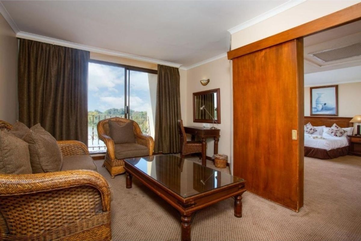 A hotel suite living area featuring carpeted flooring, a sliding wooden partition door, and access to a balcony with exterior views.