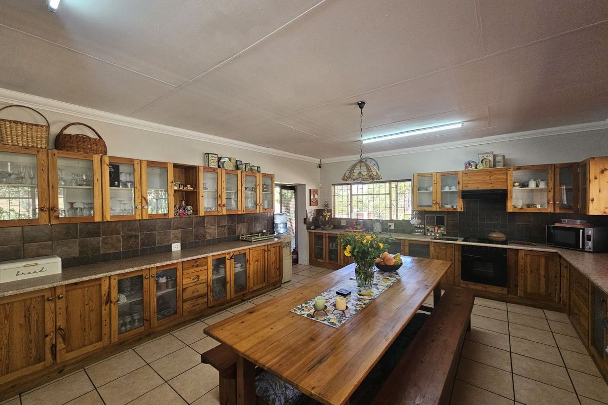 Spacious farmhouse kitchen featuring extensive wooden cabinetry, tiled flooring, built-in oven, and a large central dining area.