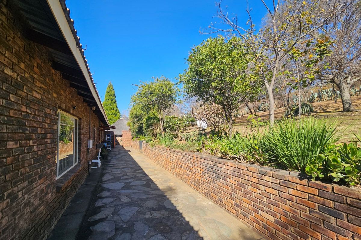 A side exterior view of the farm property featuring a stone-paved walkway, face-brick walling, and a tiered garden with established trees and shrubs.