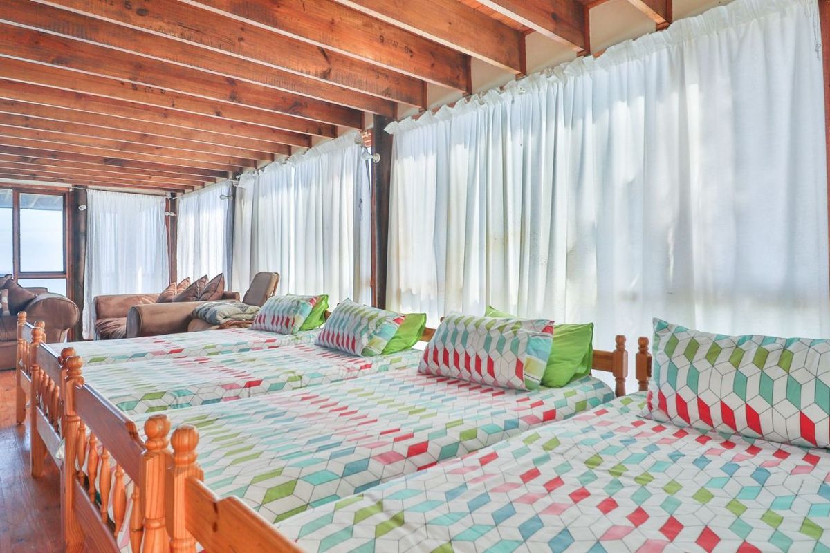 Spacious bedroom featuring exposed timber ceiling beams, warm timber flooring, and large windows allowing for ample natural light.
