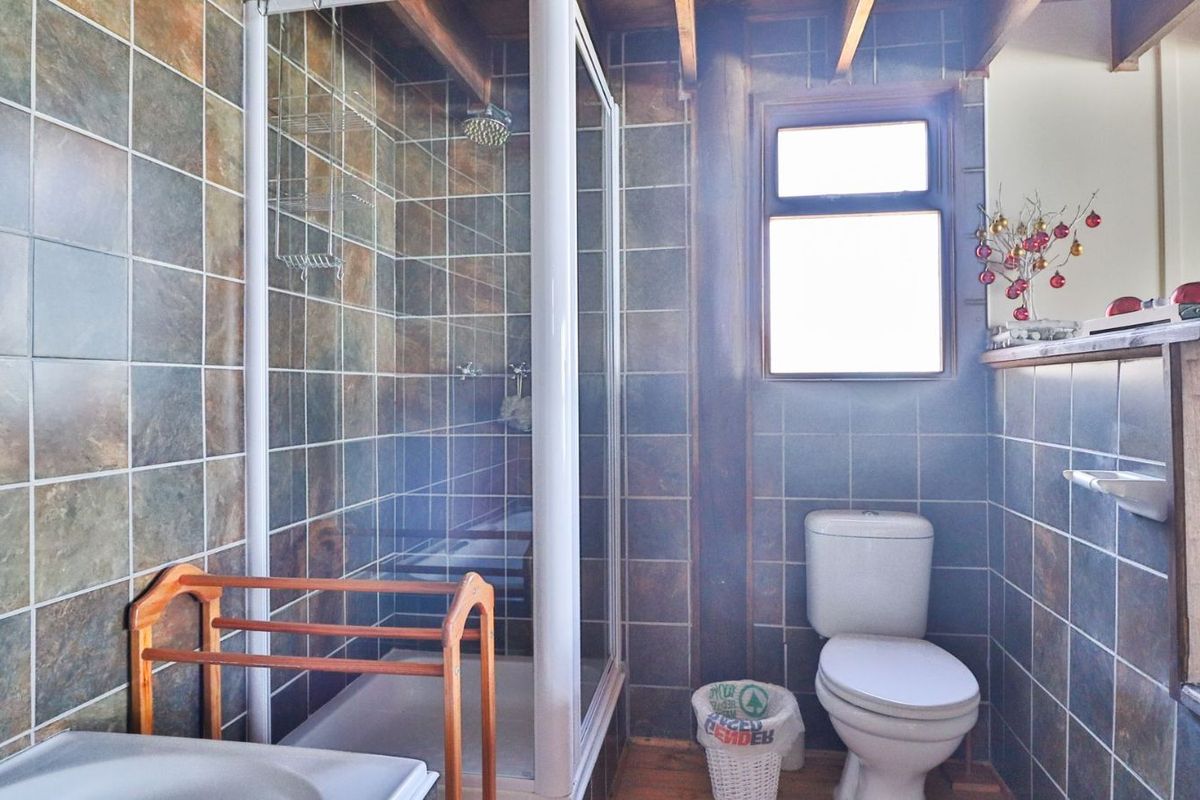 A bathroom featuring a shower enclosure, toilet, and dark slate-style wall tiling with exposed timber ceiling beams.