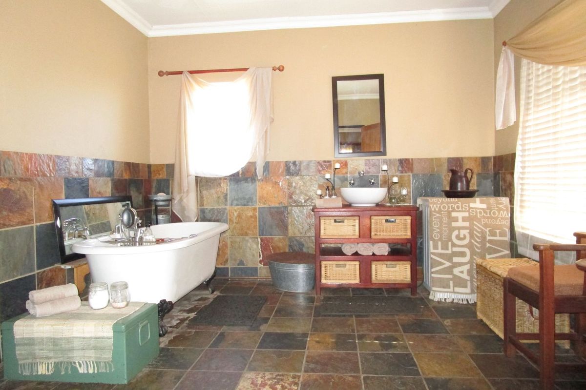 A rustic-style bathroom featuring a classic clawfoot bathtub, slate tile flooring, wall tiling, and a vanity unit with a vessel sink.