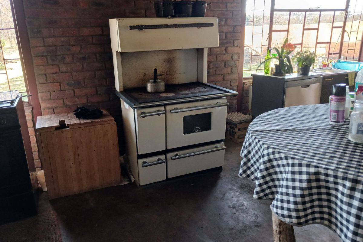 Rustic kitchen area featuring an antique-style range stove, exposed brick walls, and large industrial-style windows overlooking the farm landscape.