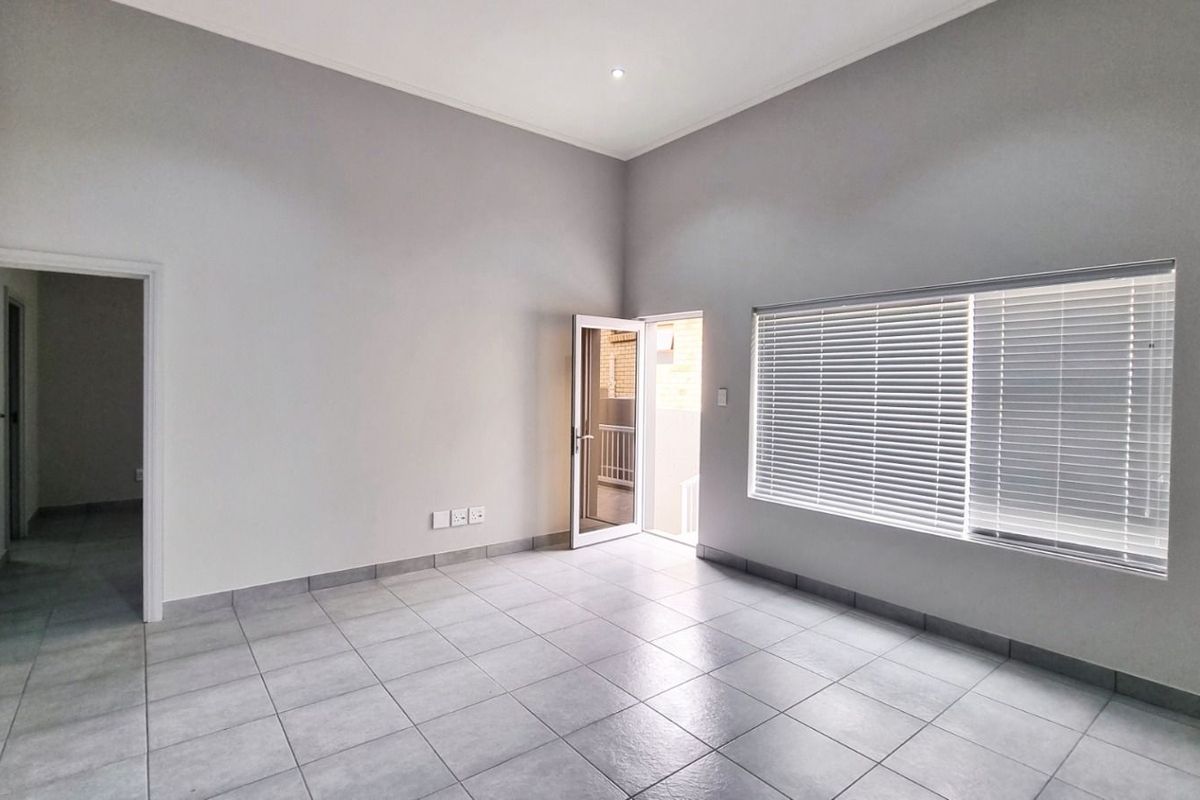 A bright, empty living room featuring neutral grey walls, tiled flooring, and a glass door providing access to an outdoor area.