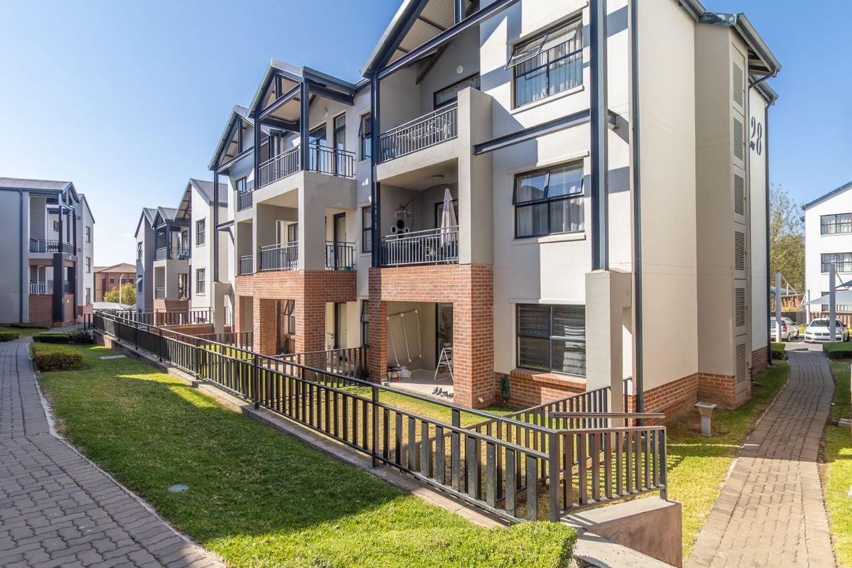 Exterior view of a modern multi-story apartment complex featuring brick and plaster facade, private balconies, and landscaped communal garden areas.