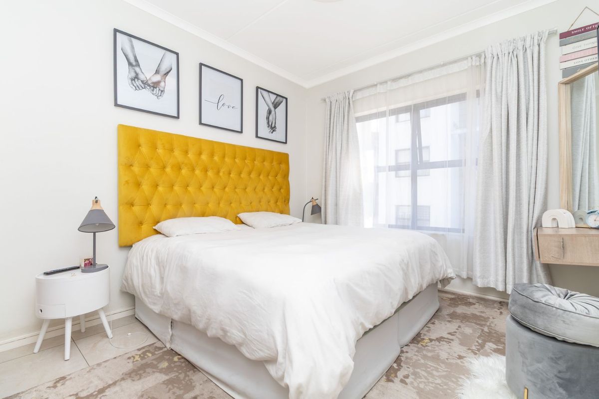 A bright and well-maintained bedroom featuring neutral walls, tiled flooring, and a large window with fitted curtains.