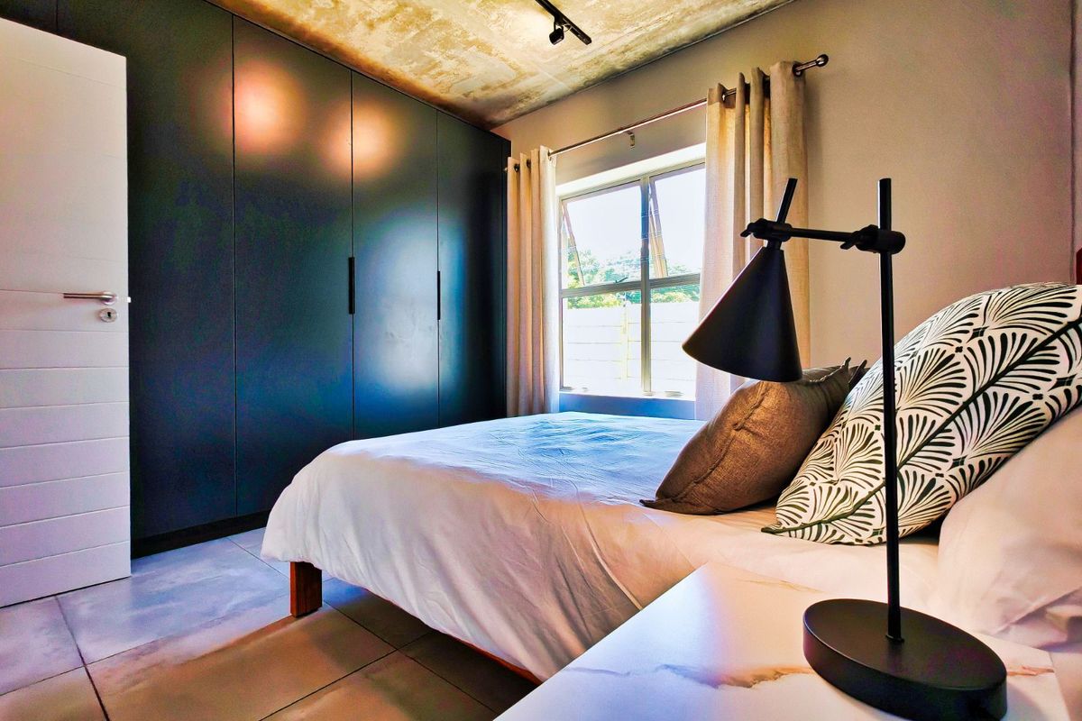 Modern bedroom featuring a raw concrete ceiling, large floor-to-ceiling built-in cupboards, tiled flooring, and a window providing natural light.
