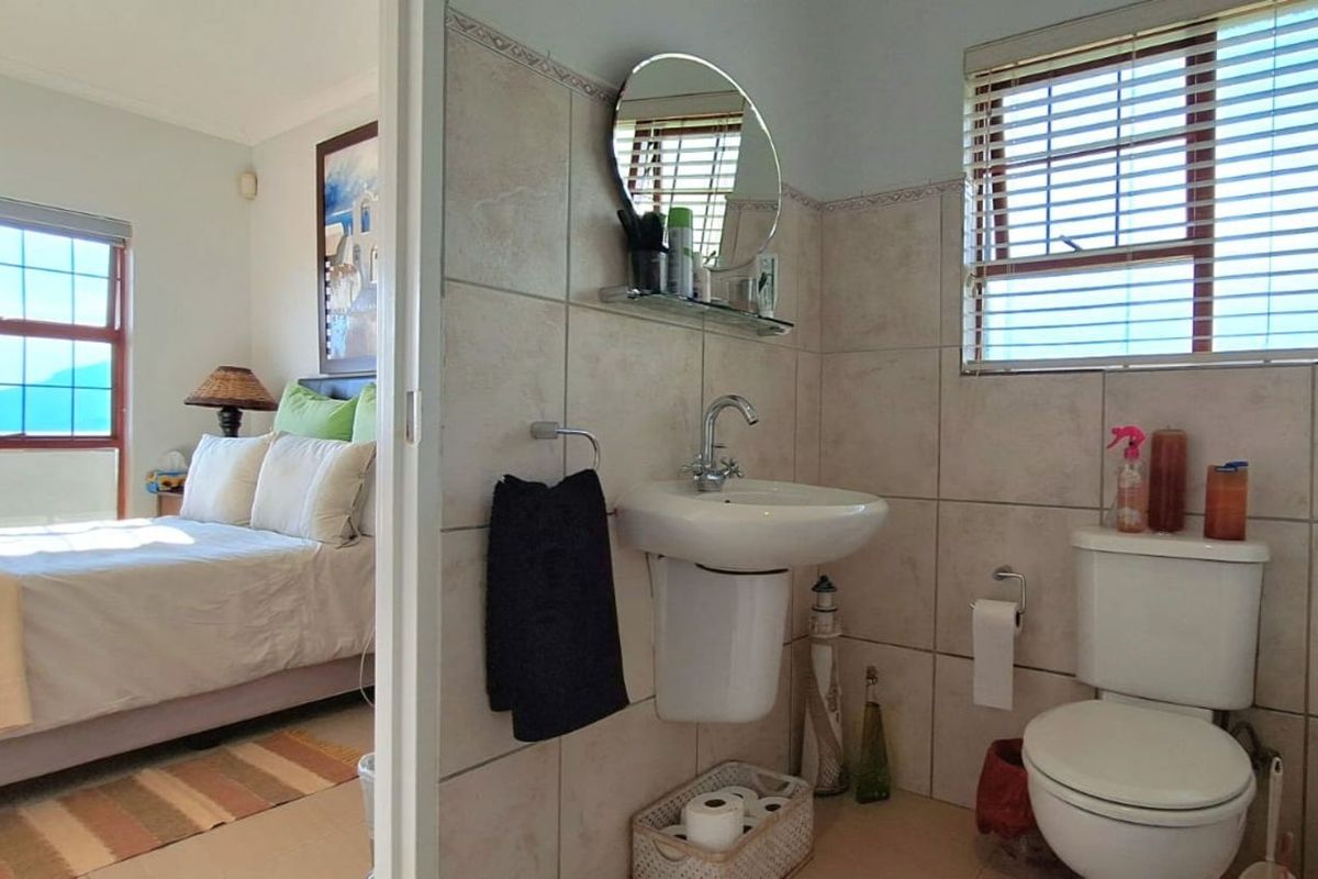 A functional bathroom featuring tiled walls, a wall-mounted basin, and a toilet, with an adjacent view into a bedroom.
