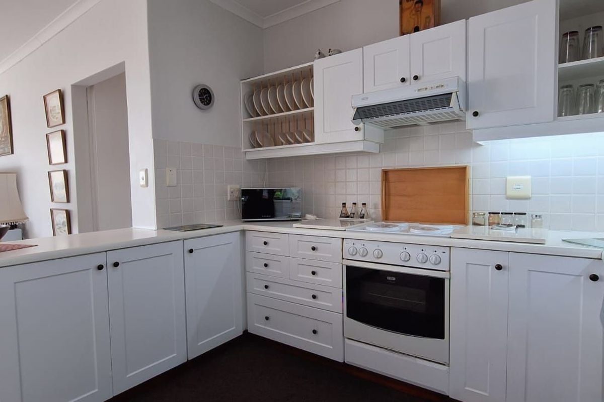 A clean and functional kitchen featuring white cabinetry, tiled splashbacks, a built-in oven, and an integrated extractor fan.