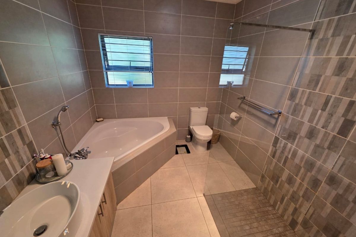 Modern bathroom featuring a corner bathtub, a glass-enclosed walk-in shower, a vanity with a vessel sink, and neutral floor-to-ceiling tiling.