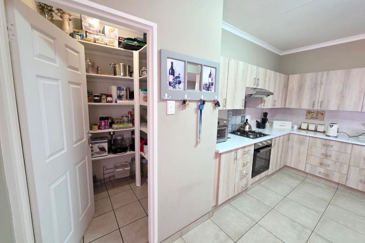 A functional kitchen featuring light wood-grain cabinetry, built-in oven and hob, and an adjacent walk-in pantry with ample shelving.
