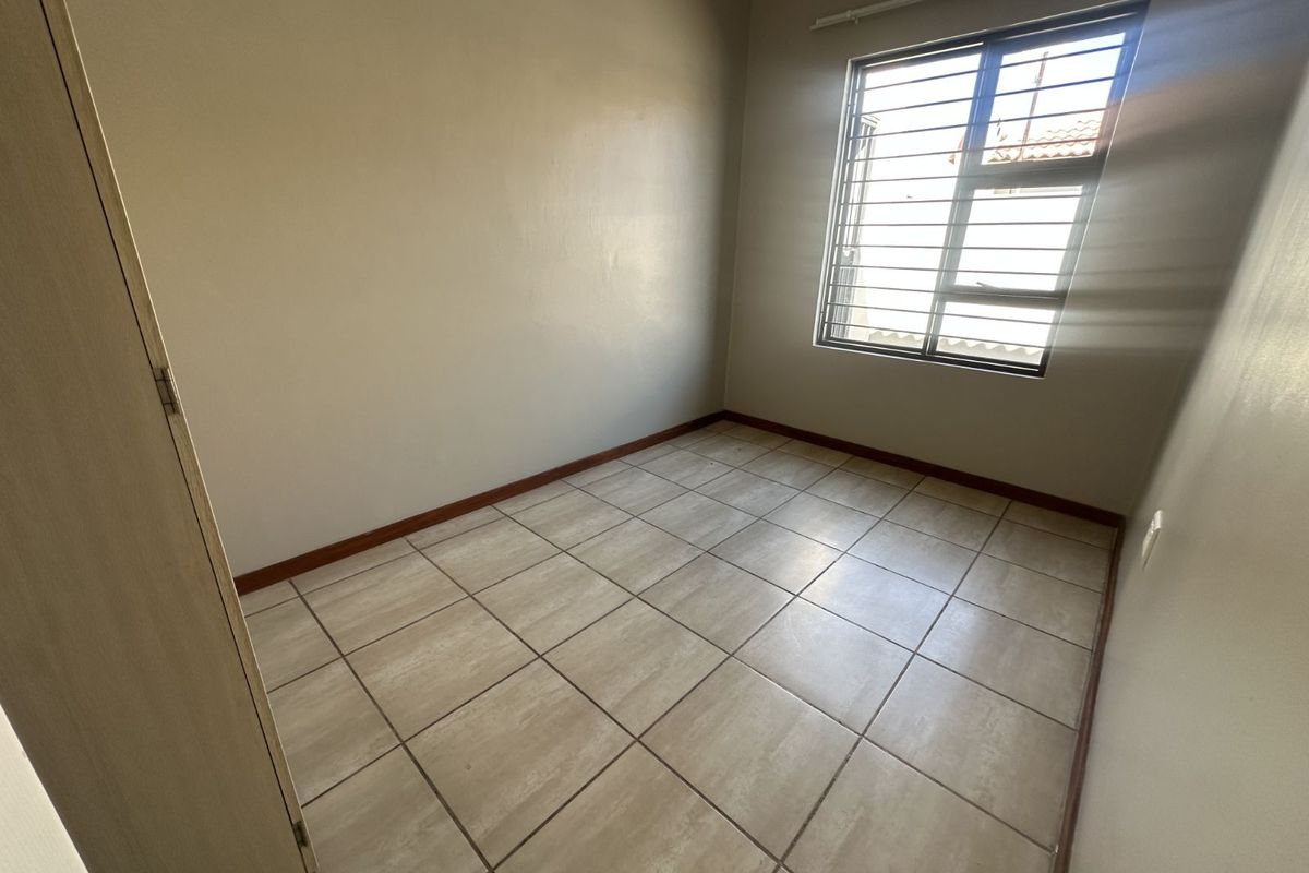 A vacant bedroom featuring neutral tiled flooring, built-in cupboard, and a window fitted with security bars.
