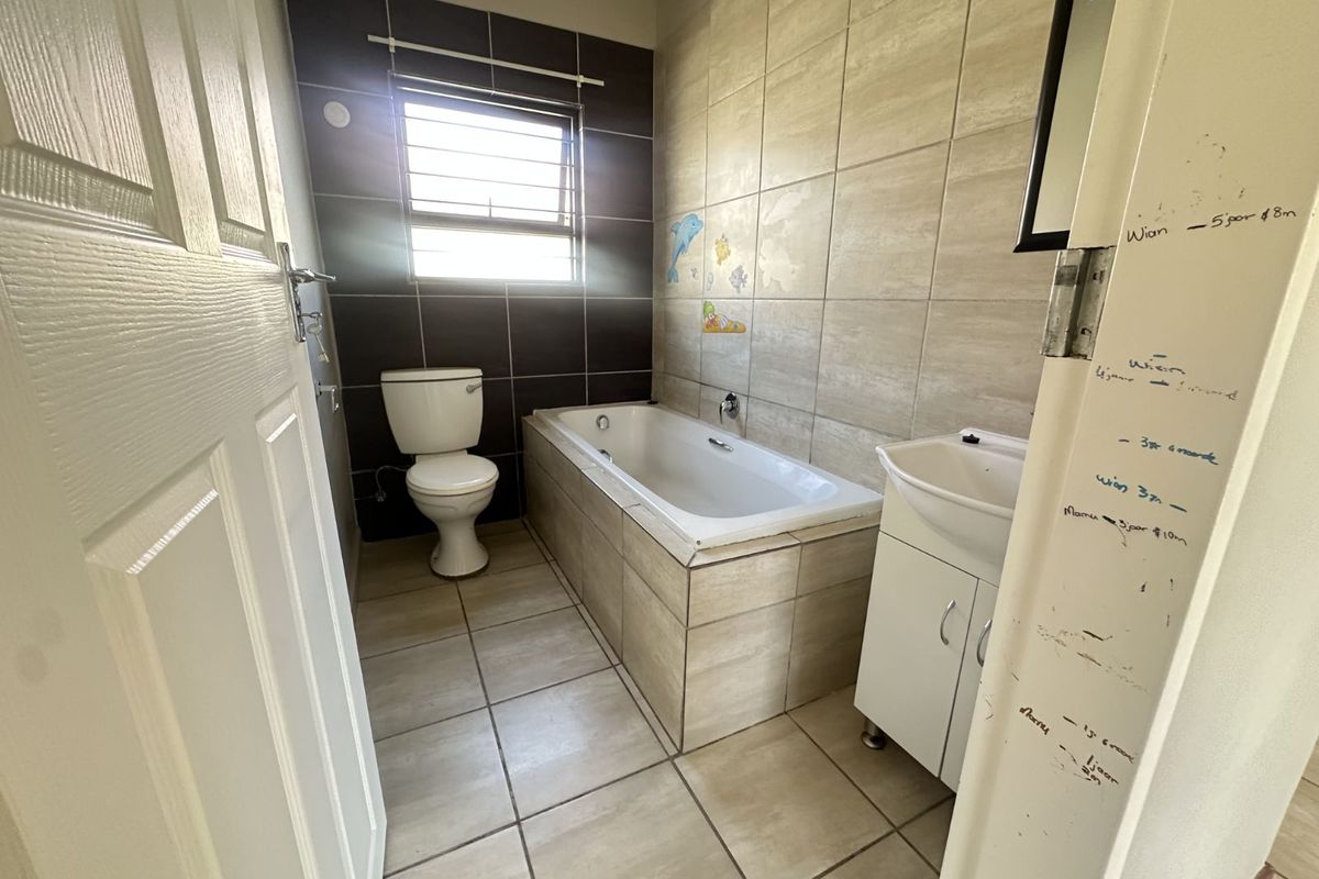 A functional bathroom featuring a built-in bathtub, pedestal vanity, and toilet with tiled walls and flooring.