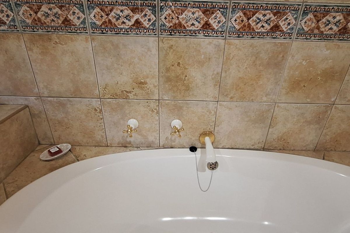 A bathroom featuring a built-in bathtub with traditional gold-tone wall-mounted taps and decorative patterned tile backsplash.