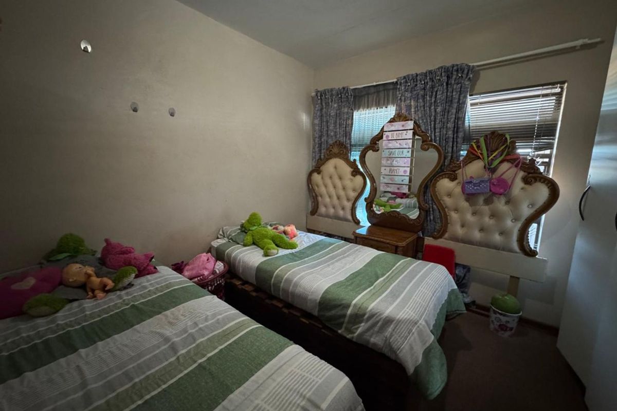 A bedroom featuring two twin beds, carpeted flooring, and a window with curtains.