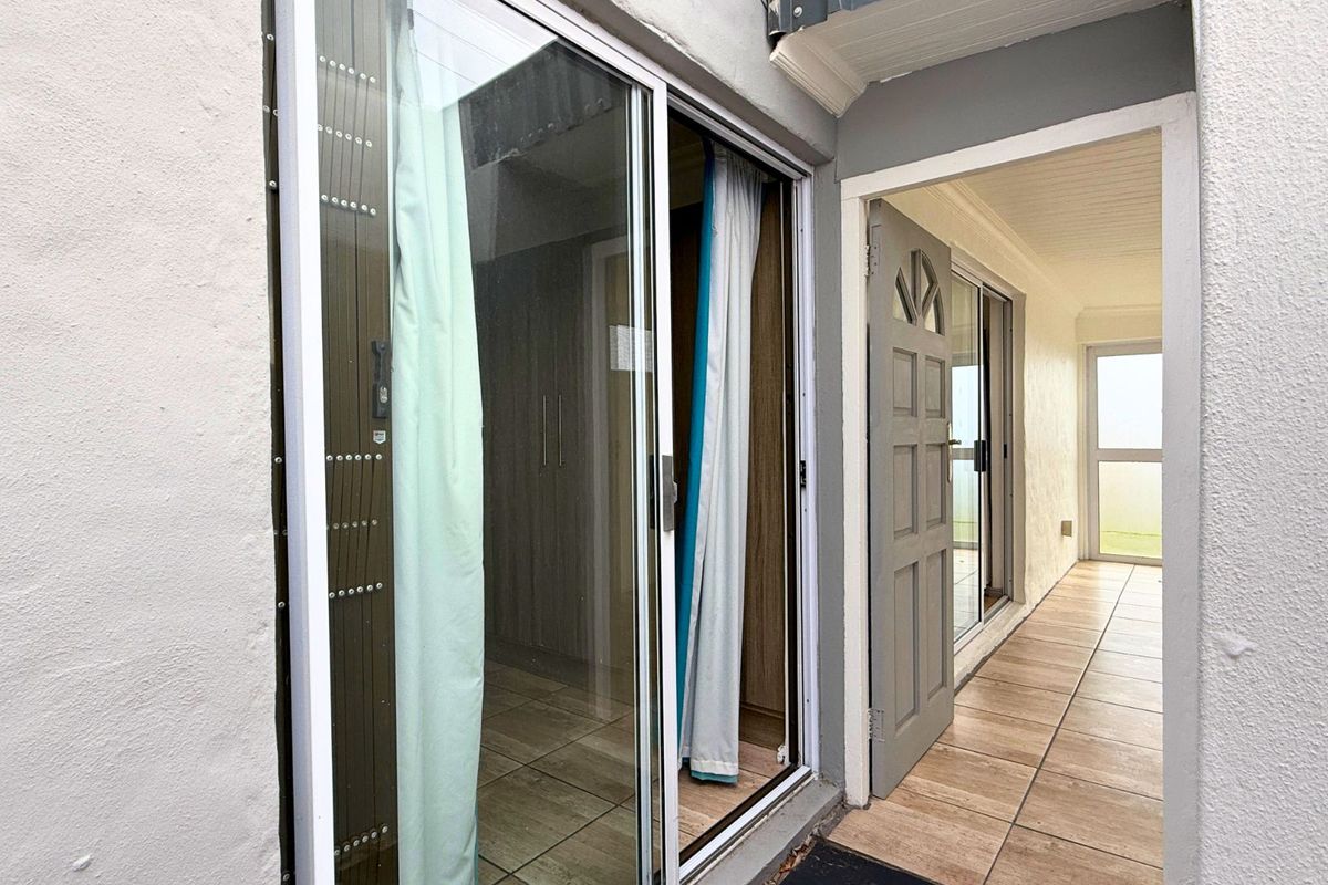 Exterior view showing a sliding glass door entrance and a tiled walkway leading to a secondary door, providing access to the interior living space.