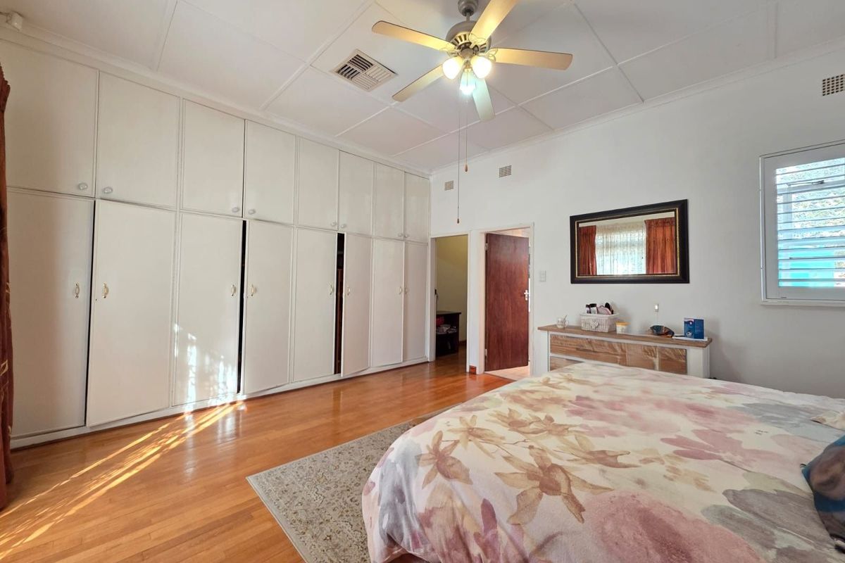 Spacious bedroom featuring extensive floor-to-ceiling built-in cabinetry, polished timber flooring, and a central ceiling fan.