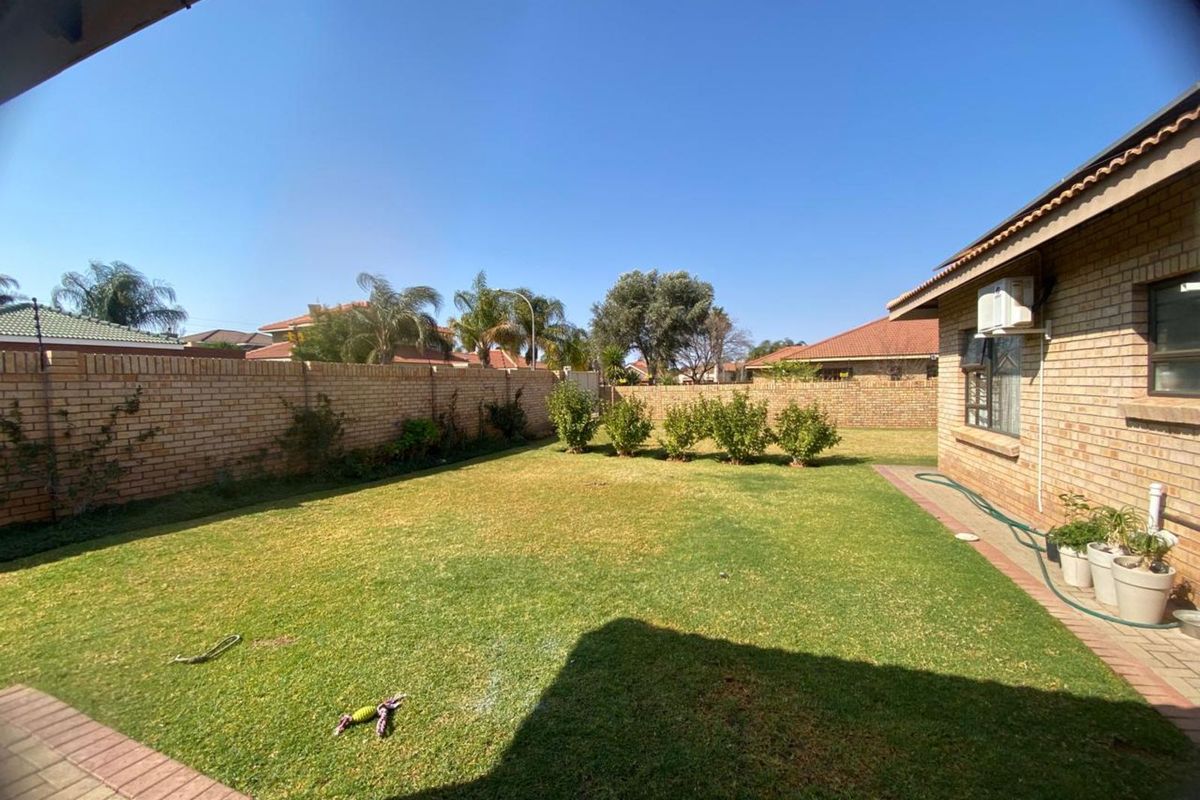 A private rear garden featuring a brick boundary wall, a lawn area, and a paved walkway adjacent to the house exterior.