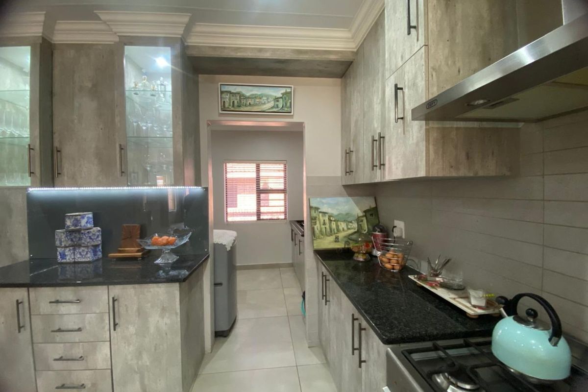 Modern kitchen featuring stone-look cabinetry, granite countertops, integrated lighting, and a stainless steel extractor fan, leading into a functional scullery area.