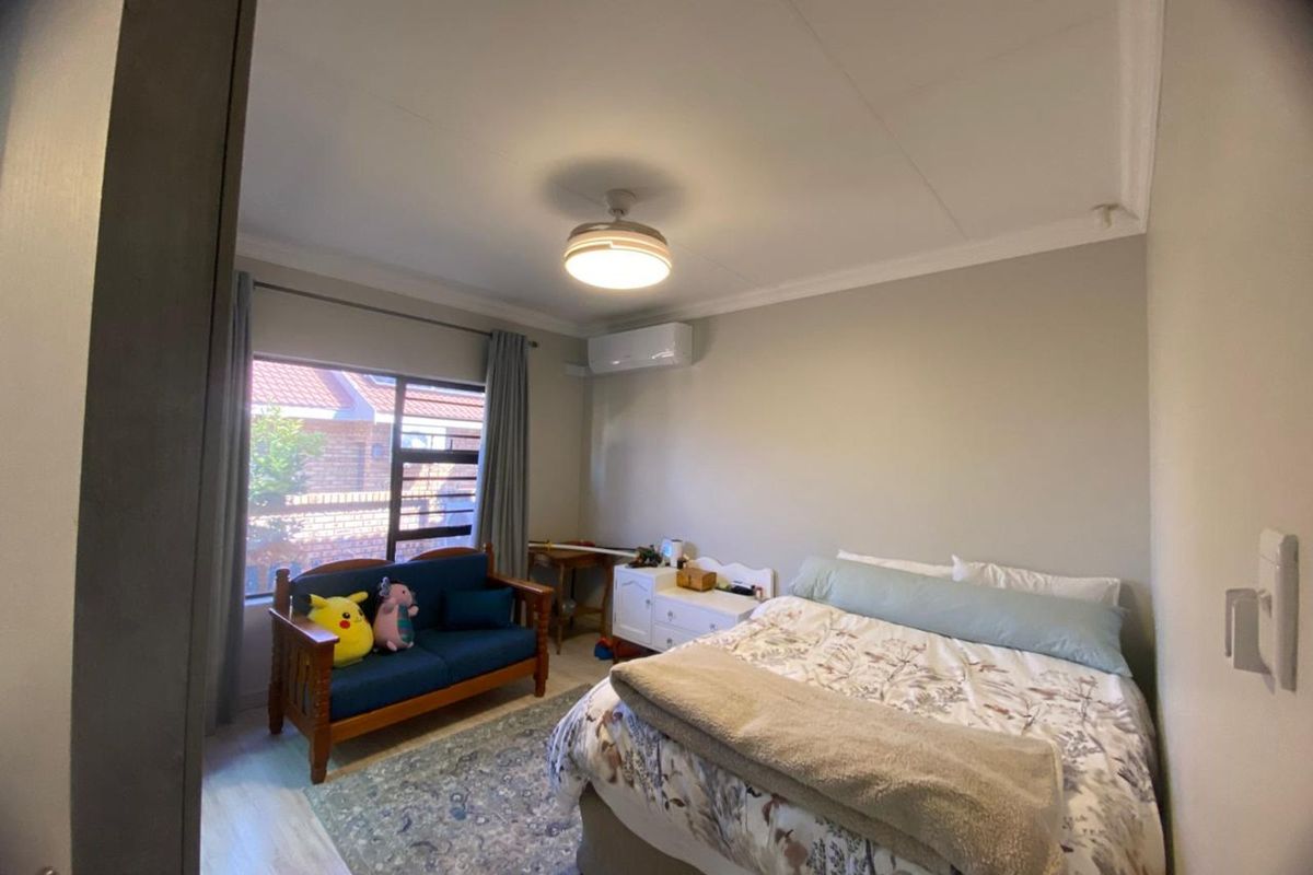 A well-lit bedroom featuring a ceiling fan, wall-mounted air conditioning unit, and large window providing natural light.