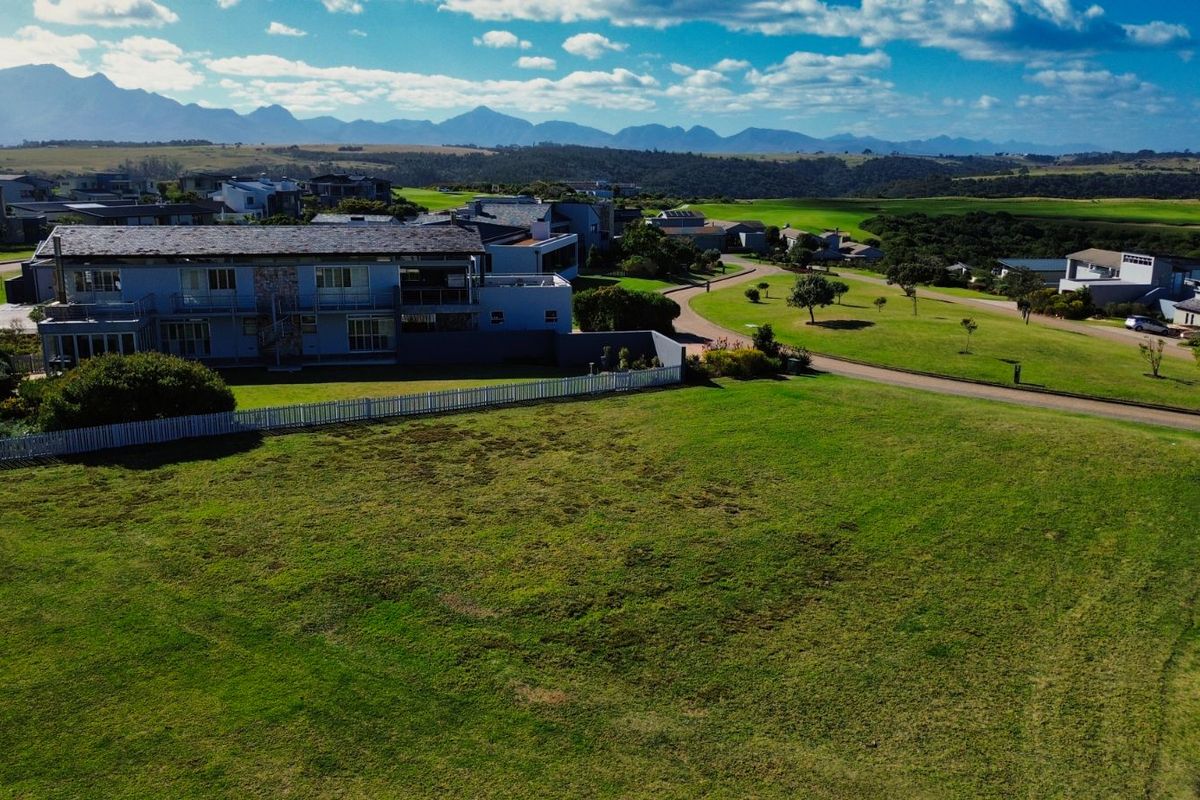 An elevated aerial view of a vacant residential plot within a landscaped estate, featuring expansive green lawns and scenic mountain views.