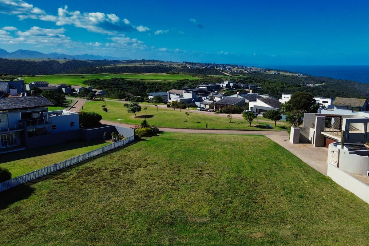 An elevated aerial view of a vacant residential plot in a coastal estate, showcasing surrounding homes and scenic landscape views.