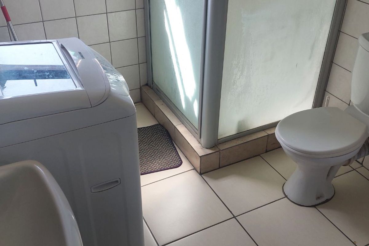 A functional bathroom featuring a shower enclosure, toilet, and basin, with tiled walls and flooring throughout.