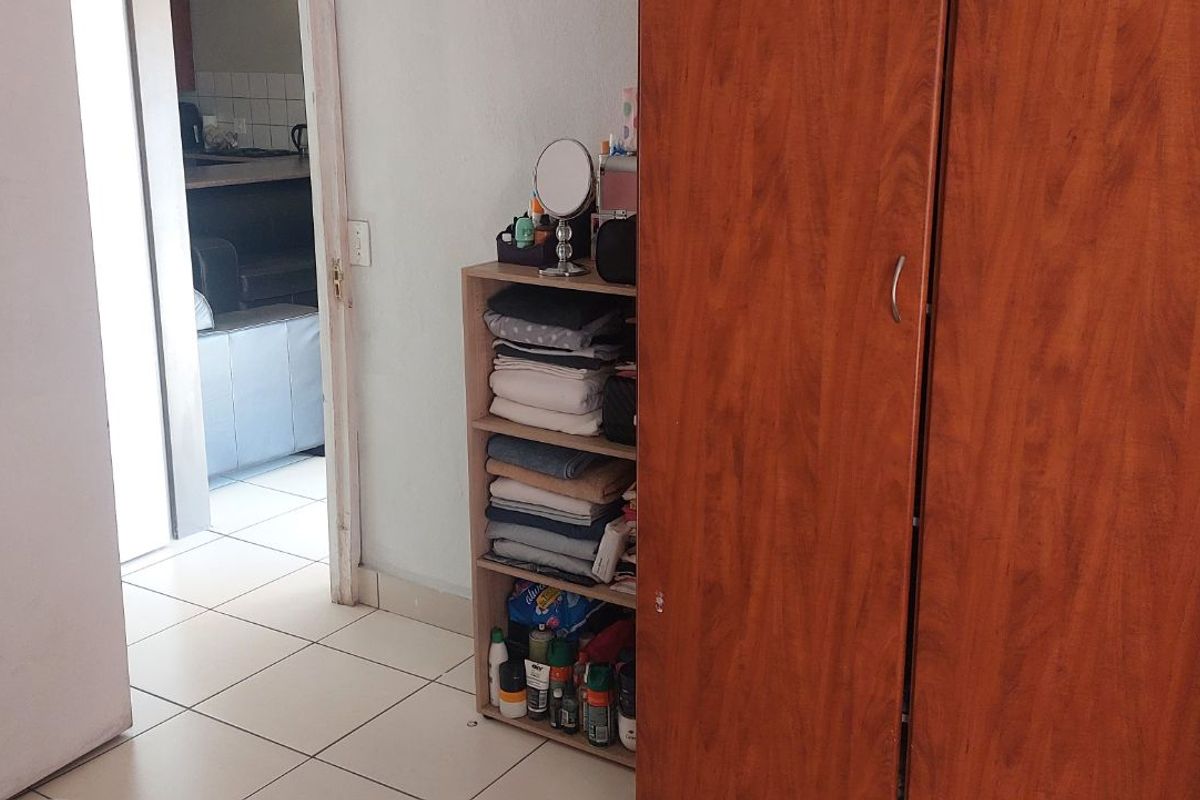 A view of a bedroom interior featuring built-in wooden cabinetry and tiled flooring, with a doorway leading to an adjacent living area.