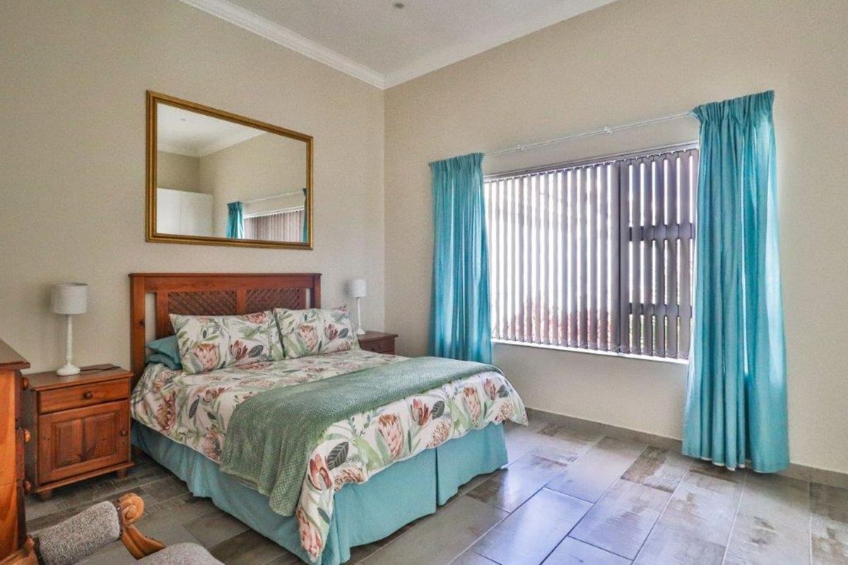 A well-lit bedroom featuring tiled flooring, large window with vertical blinds, and crown molding.