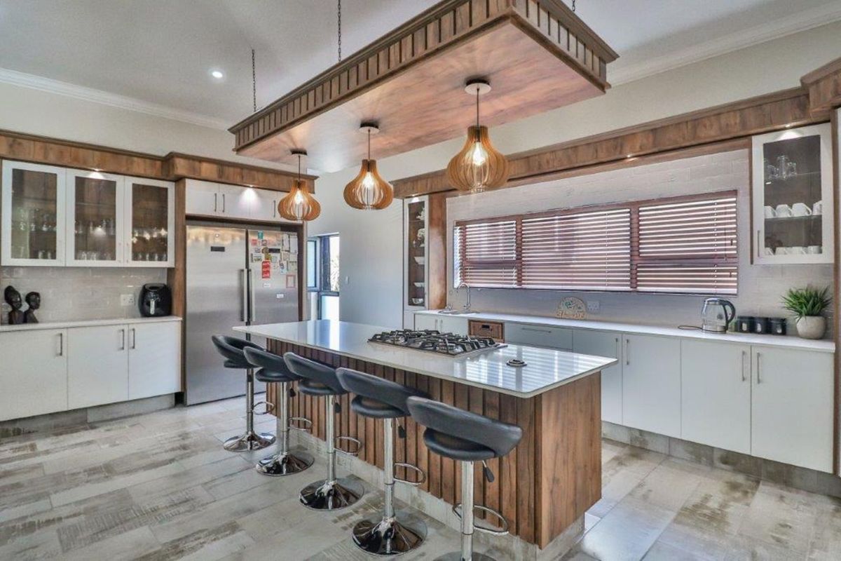 Modern kitchen featuring a large central island with a built-in gas hob, custom wooden cabinetry, stone countertops, and a decorative suspended timber ceiling feature.