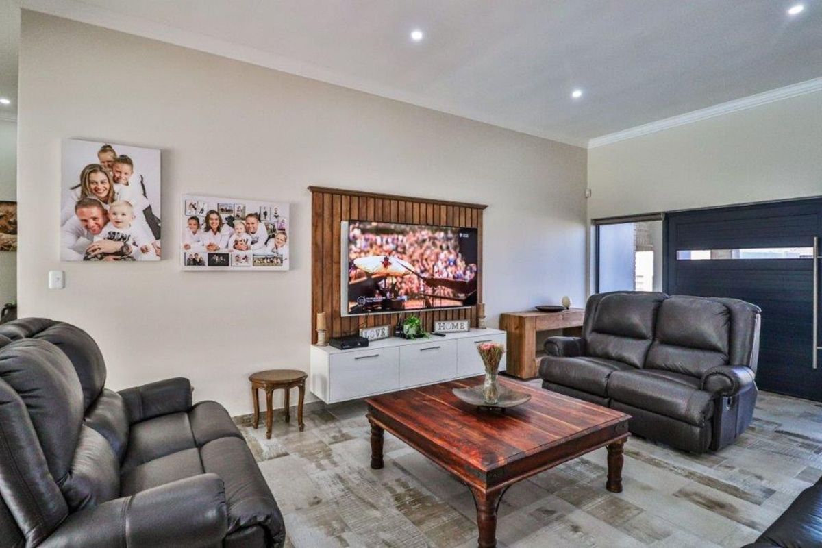 A well-maintained living room featuring a decorative timber-paneled feature wall with integrated media storage and recessed ceiling downlights.
