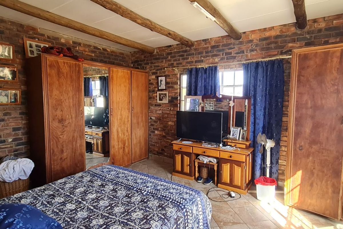 A rustic bedroom featuring exposed brick walls, timber ceiling beams, and built-in wooden wardrobes, with an adjoining en-suite bathroom.