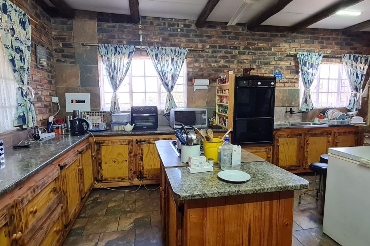 Rustic farmhouse kitchen featuring exposed brick walls, timber ceiling beams, granite countertops, a central island, and built-in oven.