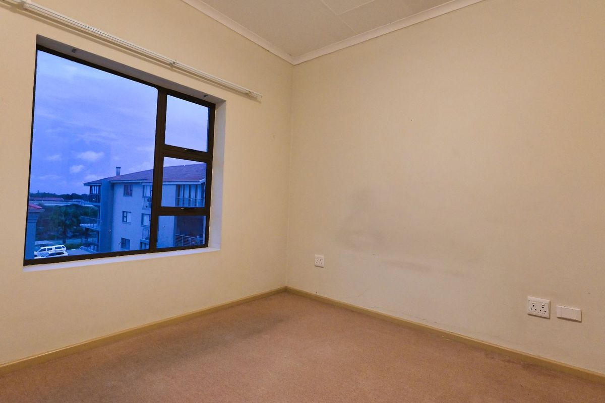 An empty bedroom featuring neutral walls, carpeted flooring, and a large window providing natural light and an exterior view.